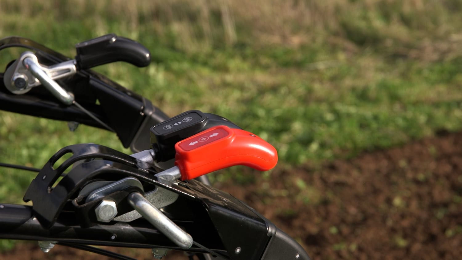 The AFT-e1 handlebar with its red throttle lever and gear lever, freshly worked soil behind