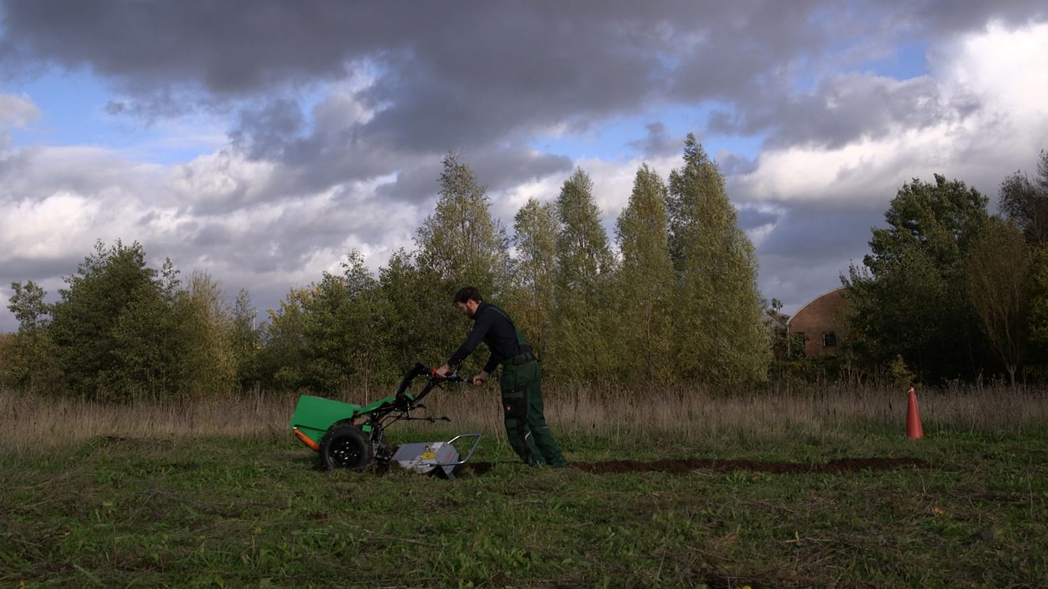 An operator working the Aftrak tractor across a field under a dark sky, soil turning behind the machine