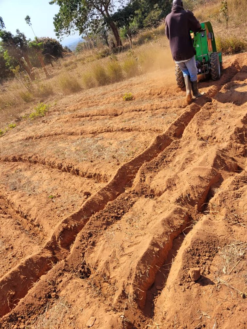 An operator working the Aftrak tractor across a slope of red soil, deep ridges formed behind it
