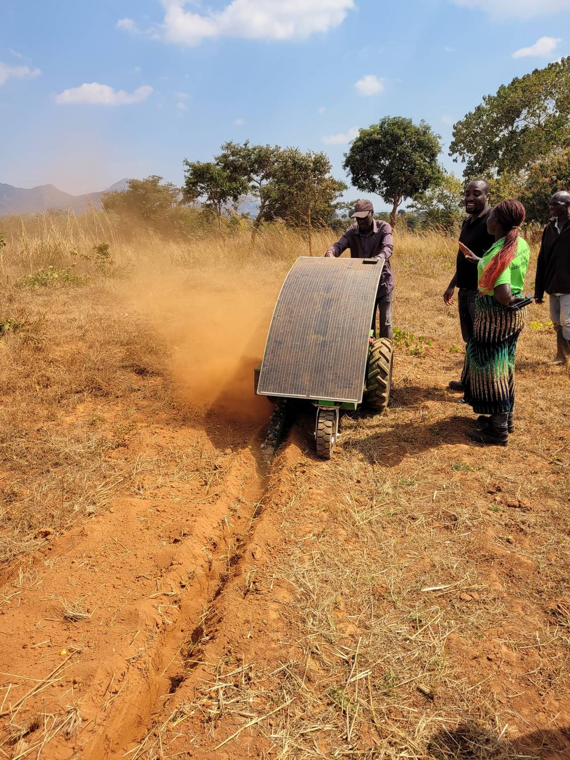 The Aftrak tractor ploughing with a solar panel mounted over it, throwing up a plume of red dust, onlookers to one side