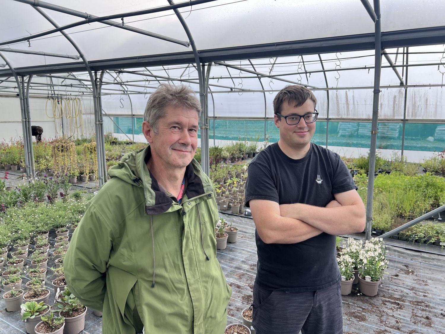 Andrew and James Lay standing in a nursery polytunnel surrounded by potted plants