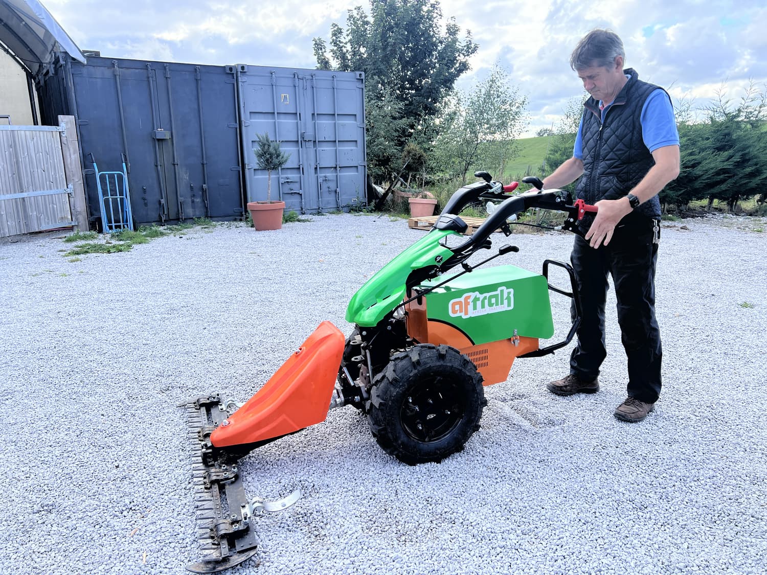The Aftrak tractor with the cutter bar fitted, standing on the gravel yard at Austwick, an operator at the handlebars and a shipping container behind