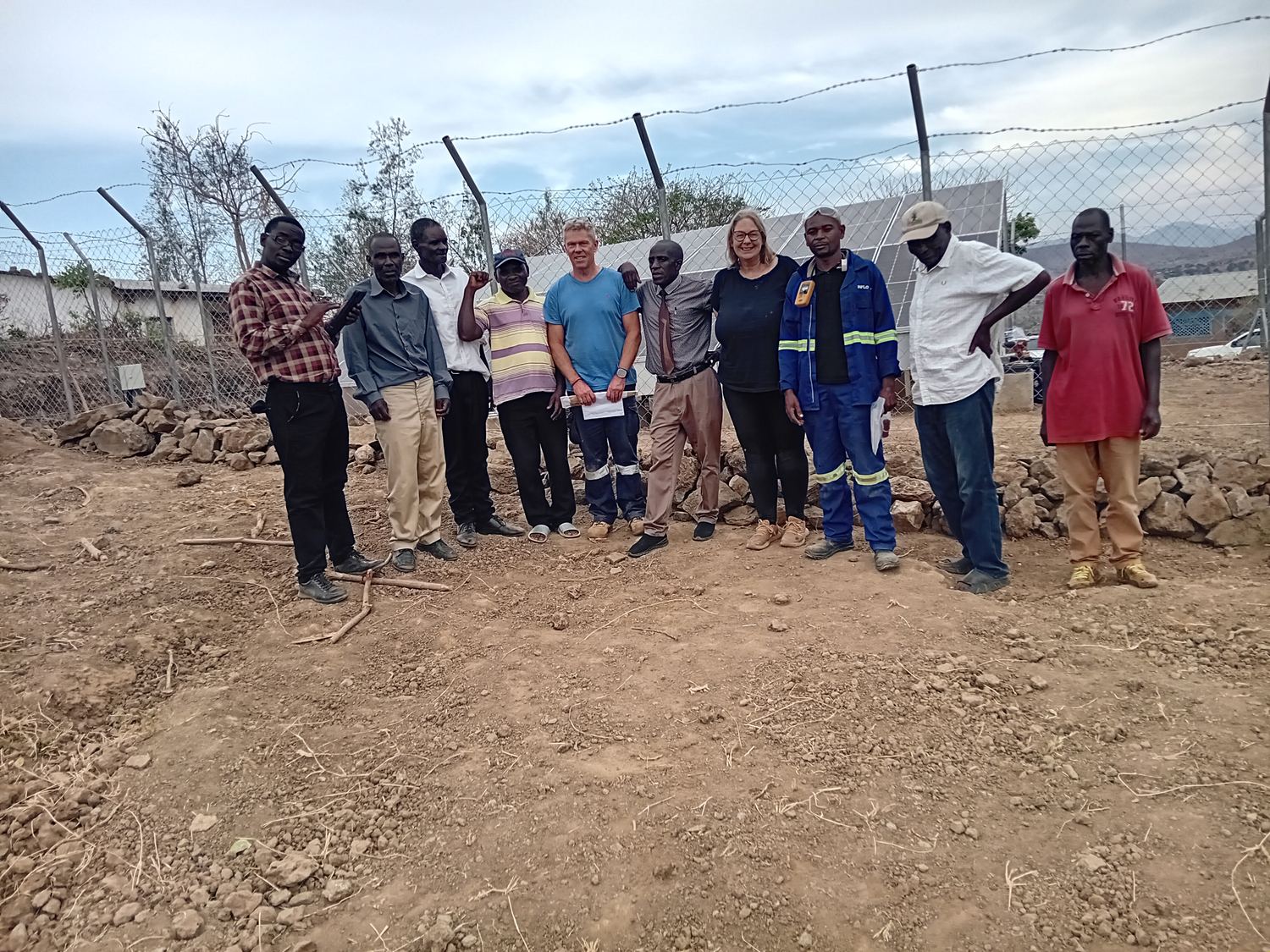 A group of people standing together in front of the fenced solar array at the school