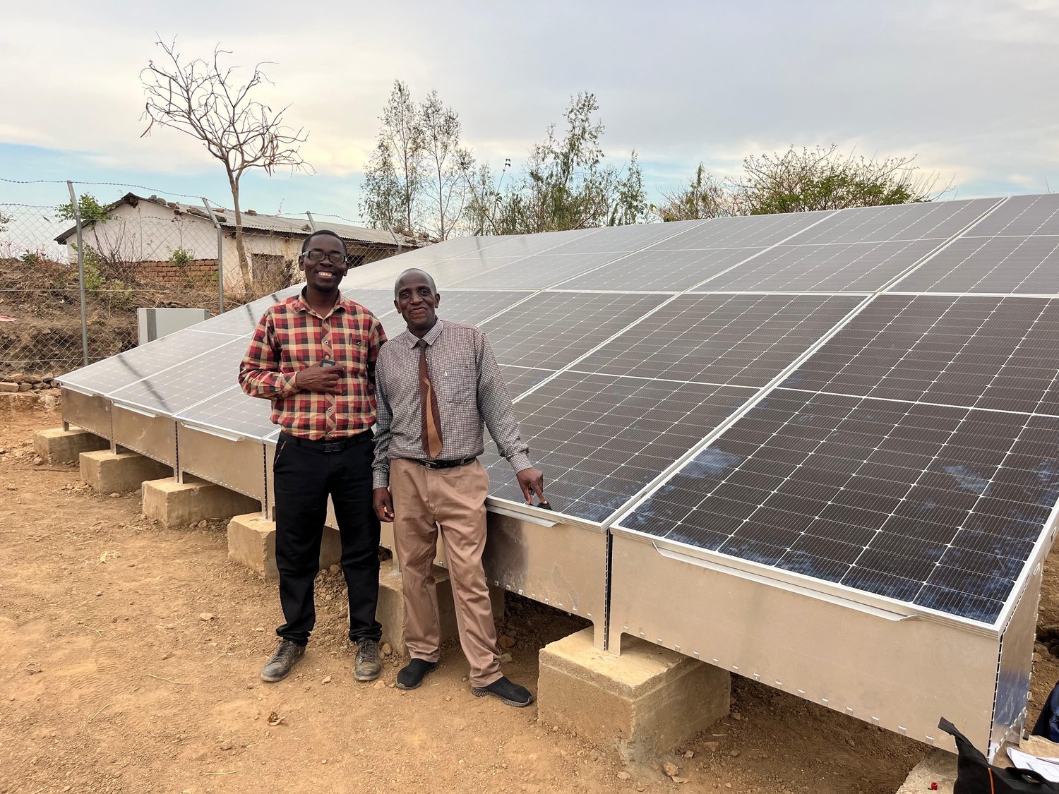 Two men standing beside the completed ground-mounted solar array, panels running away behind them