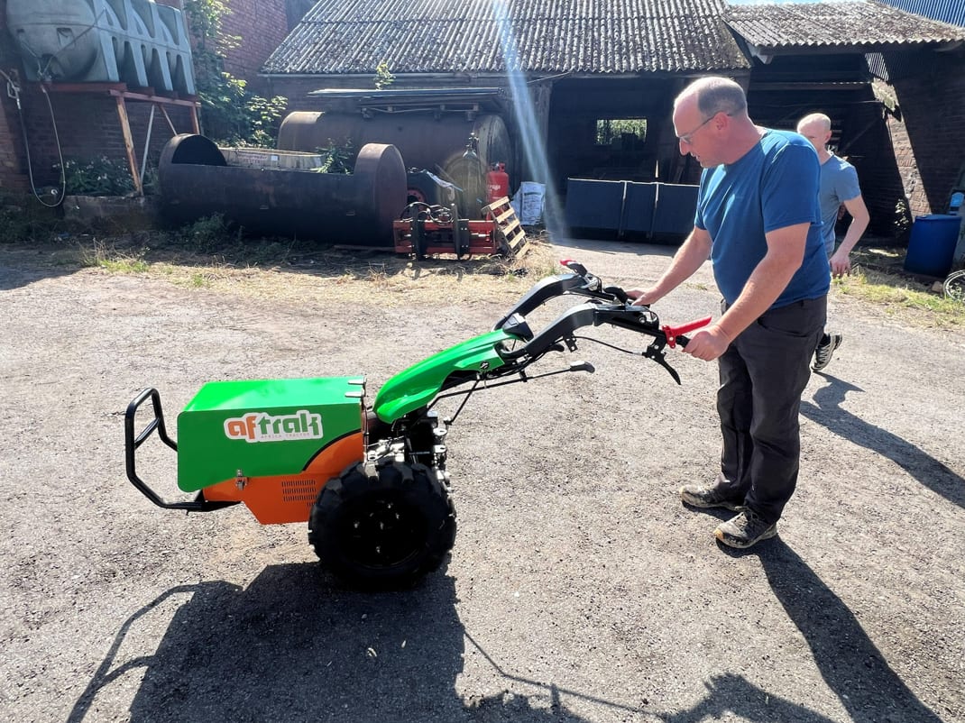 A grower taking the Aftrak tractor's handlebars for the first time in a farmyard, a second man walking across behind him