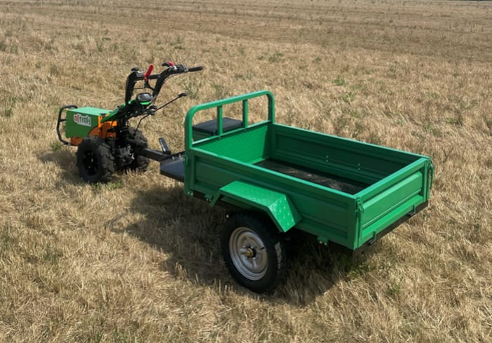 An Aftrak tractor coupled to its green tipping trailer in a stubble field