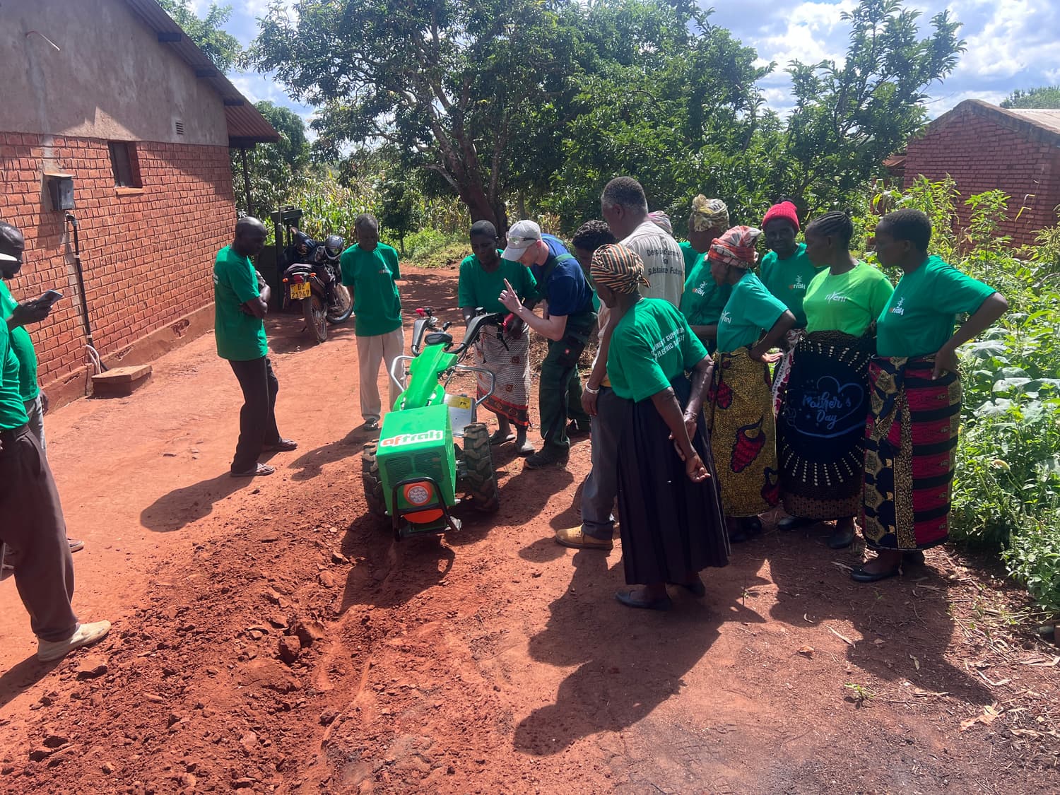 The Aftrak team in green shirts and community members gathered around the AFT-e1 on a red-earth track beside a brick building in Malawi